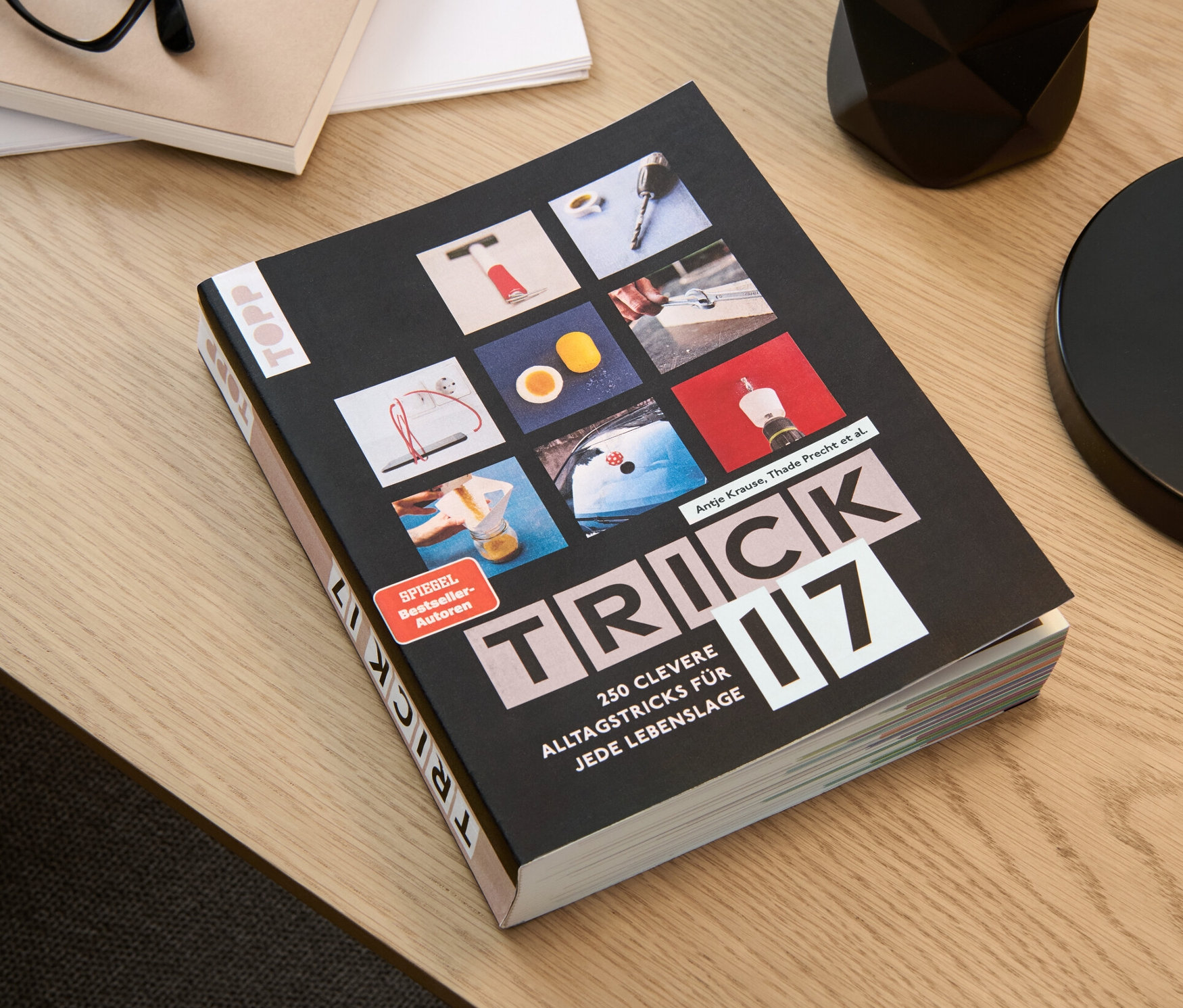 Das Buch "Trick 17" liegt auf einem Tisch neben einer Brille, einem Notizblock und einem Stifthalter.
