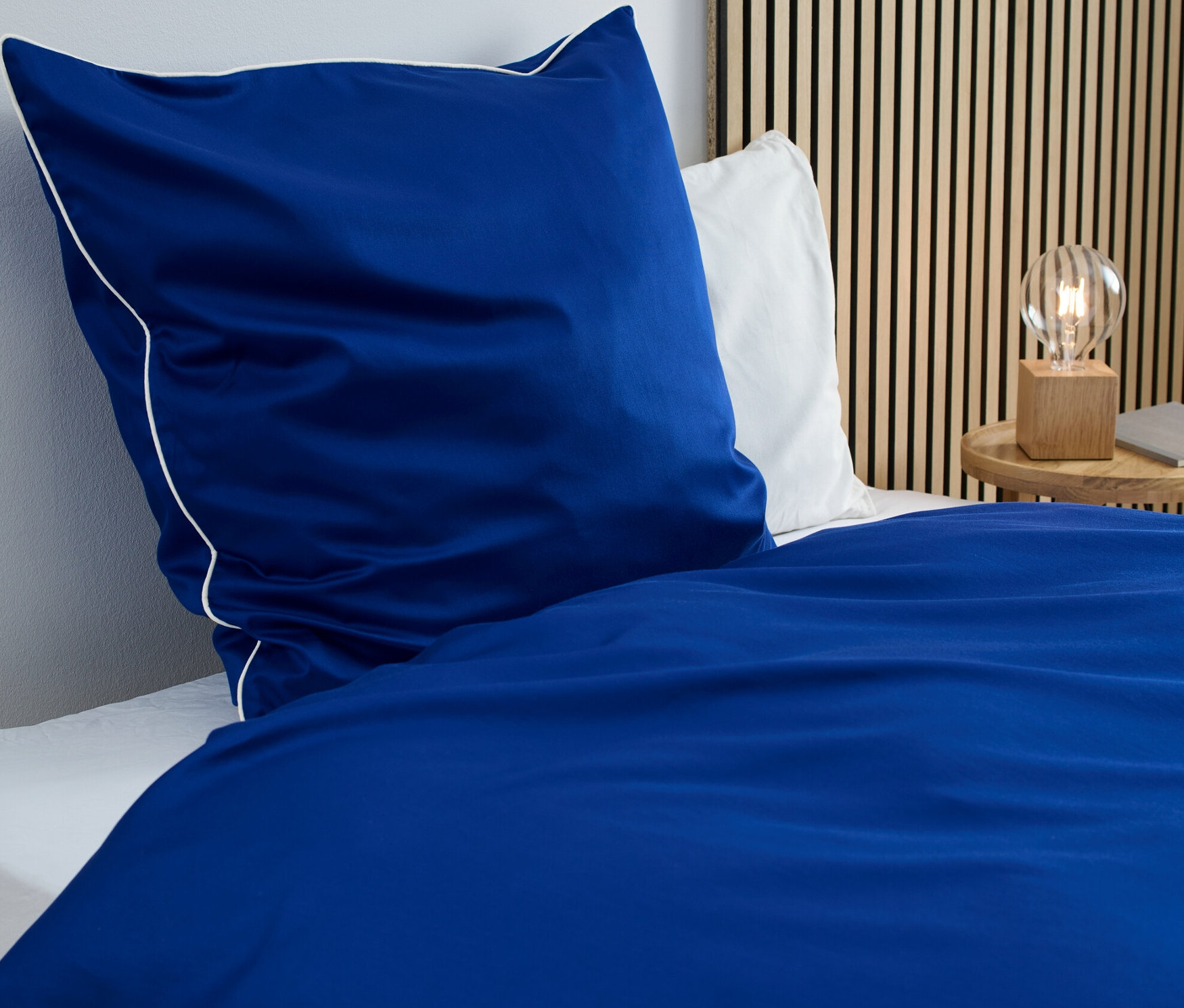 Blaue Satin-Bettwäsche in Normalgröße mit weißer Bordüre auf einem Bett.