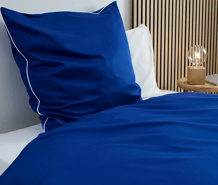 Blaue Satin-Bettwäsche in Normalgröße mit weißer Bordüre auf einem Bett.