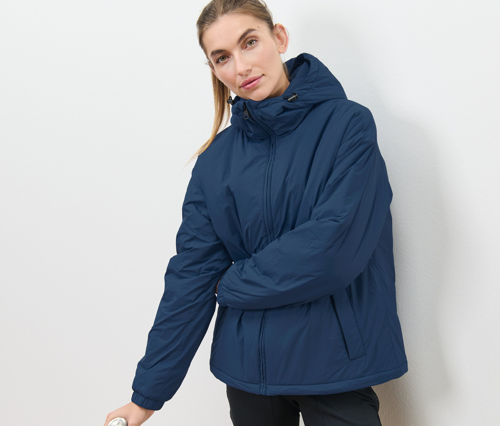 Frau posiert in Kapuzen-Jacke und hält eine Wasserflasche.