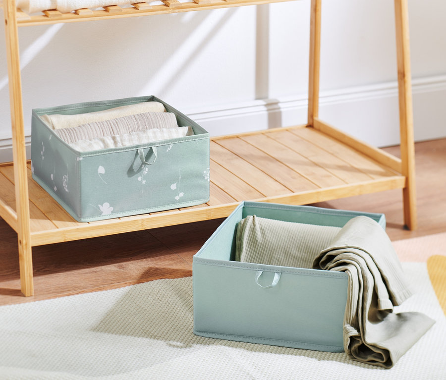 Zwei große Schubladen-Ordnungsboxen stehen auf einem Holzregal und einem Teppich.