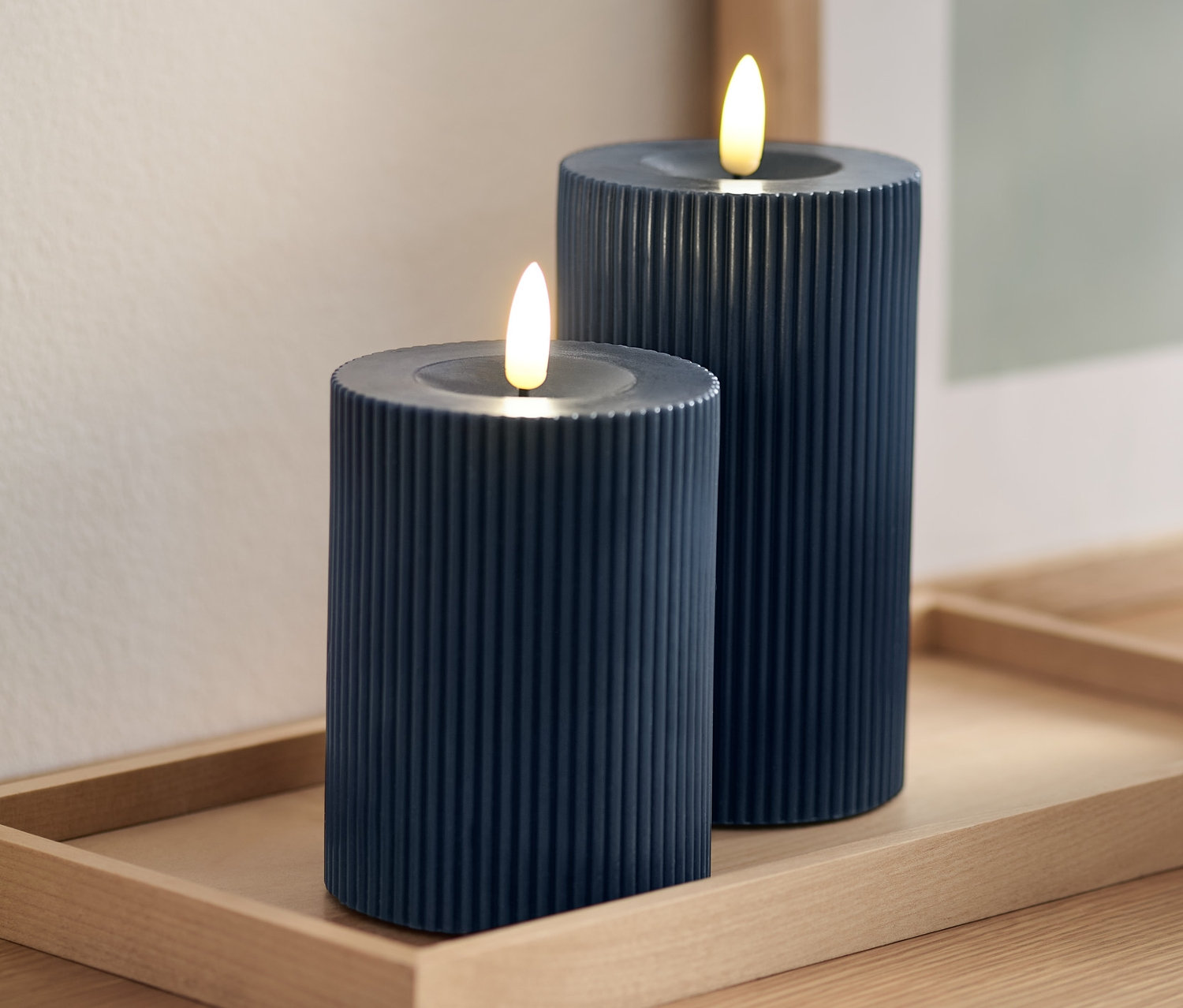 Zwei blaue LED-Echtwachskerzen auf einem Holztablett.