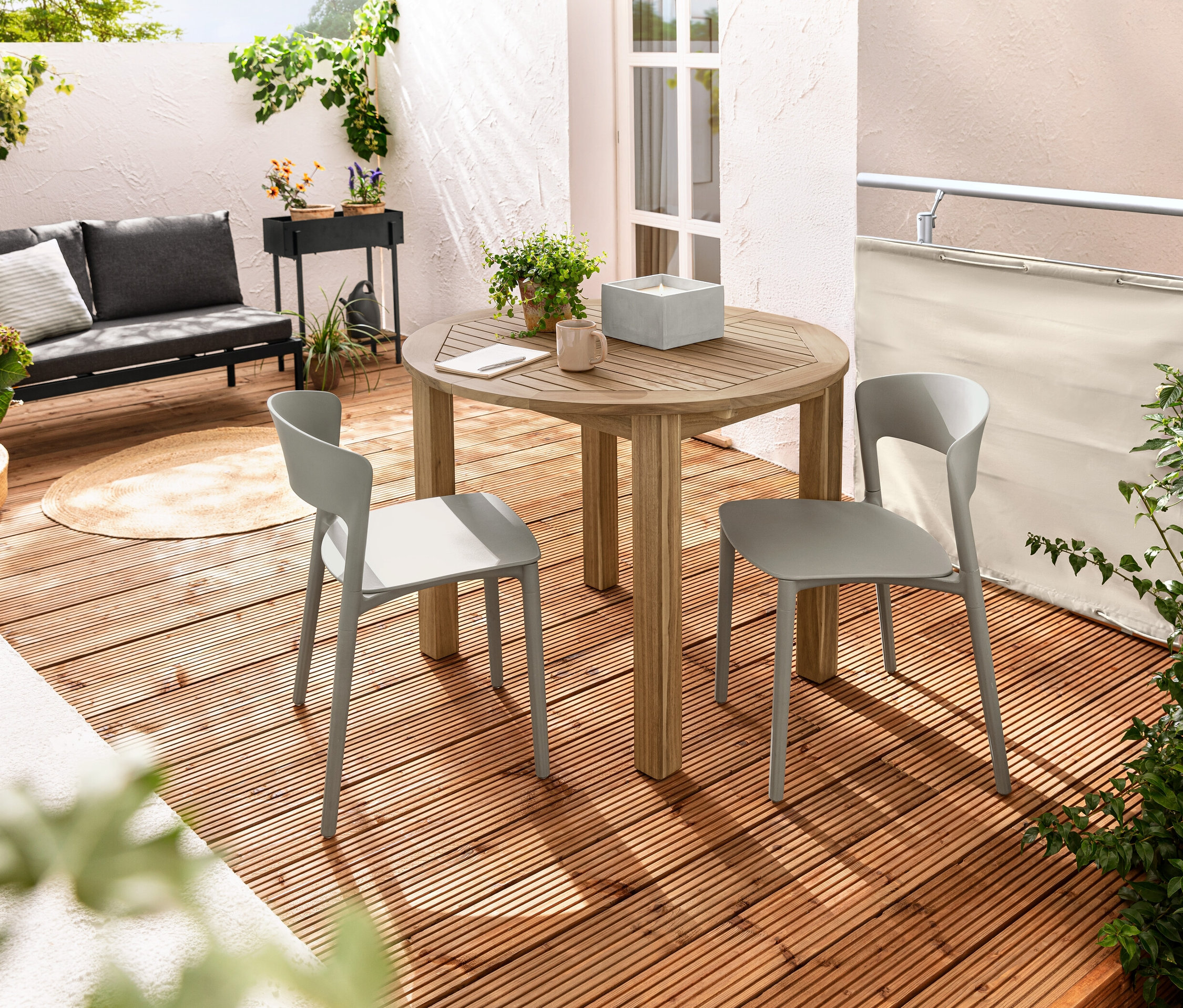 Zwei Kunststoff-Stühle stehen an einem runden Ausziehtisch auf einem Balkon. Auf dem Tisch steht eine XL-LED-Echtwachskerze im Betontopf. Ein Balkon Sicht- und Windschutz, creme, ist im Hintergrund zu sehen.