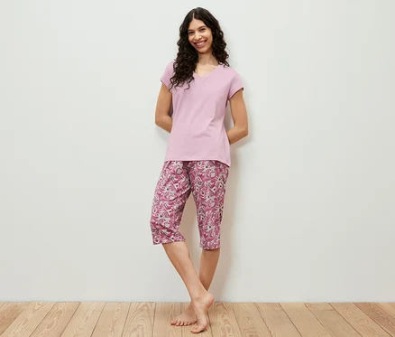 Frau posiert auf Holzboden in einem rosa 3/4-Pyjama-Set.