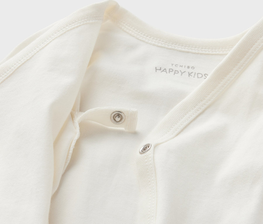 Detailansicht eines weißen 5 Baby-Bodys mit Mitwachsfunktion mit Druckknöpfen.