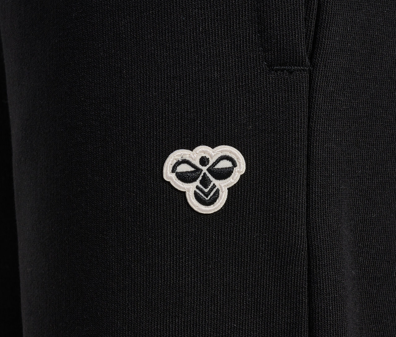 Detailaufnahme einer schwarzen HUMMEL HMLJR Loose WL Trainingshose mit Logo.