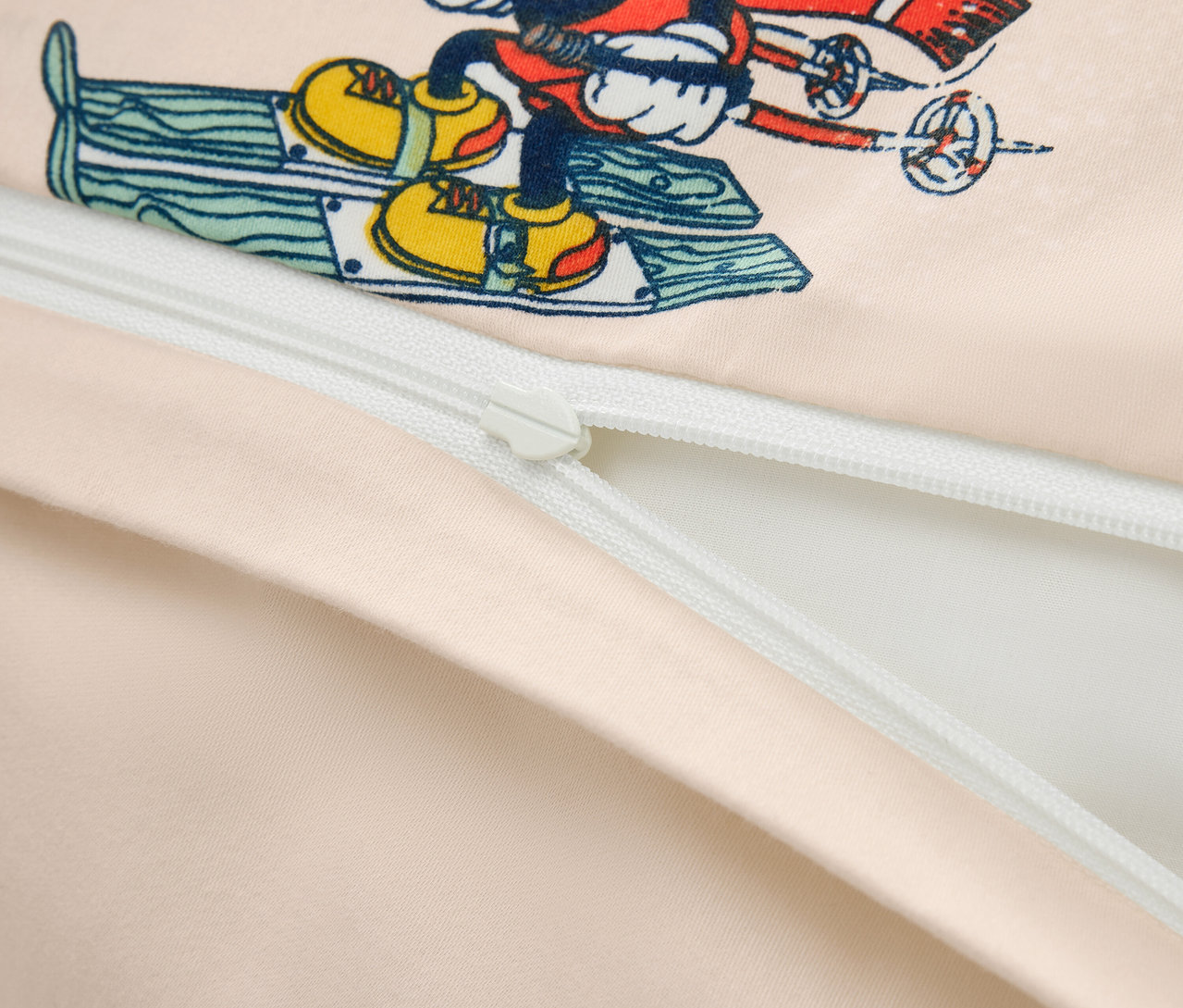 Detailaufnahme eines Bettbezugs mit einem Aufdruck von Mickey Mouse auf Skiern und einem teilweise geöffneten Reißverschluss.