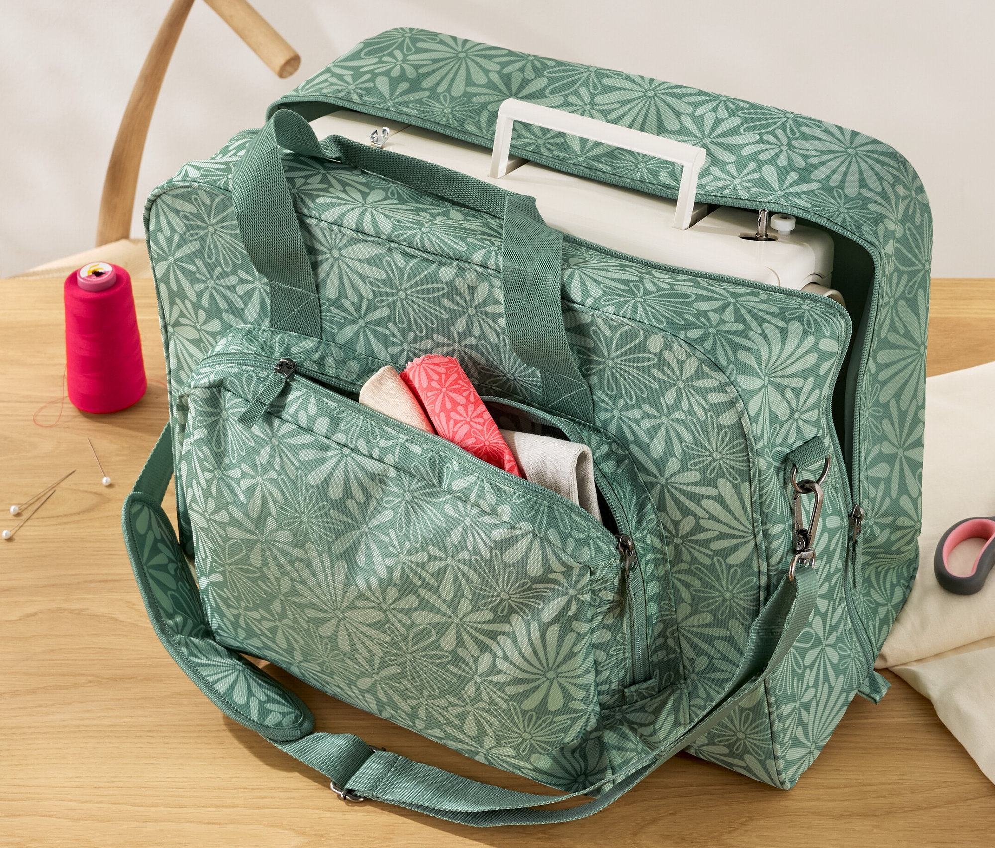 Grüne Nähmaschinentasche mit Blumenmuster auf einem Holztisch.