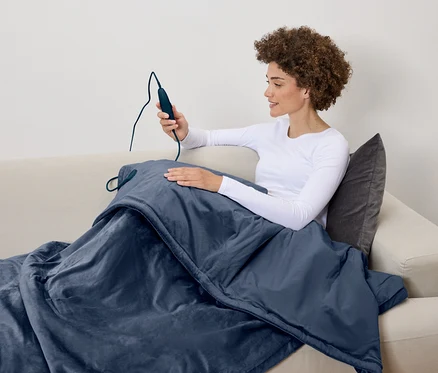 Frau sitzt auf der Couch und hält die Fernbedienung einer Heizdecke.