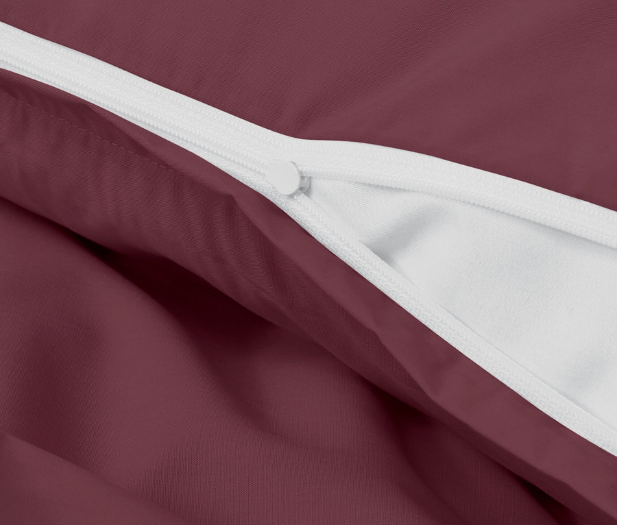 Detailaufnahme eines bordeauxfarbenen Bettbezugs mit weißem Reißverschluss.