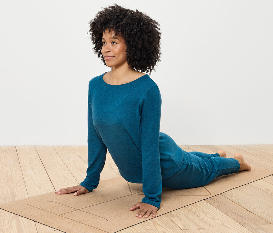 Frau mit lockigem Haar macht Yoga in blauer Kleidung auf einer Matte.