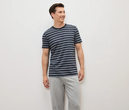 Ein Mann steht und trägt ein blau-grau gestreiftes T-Shirt und graue Hosen.