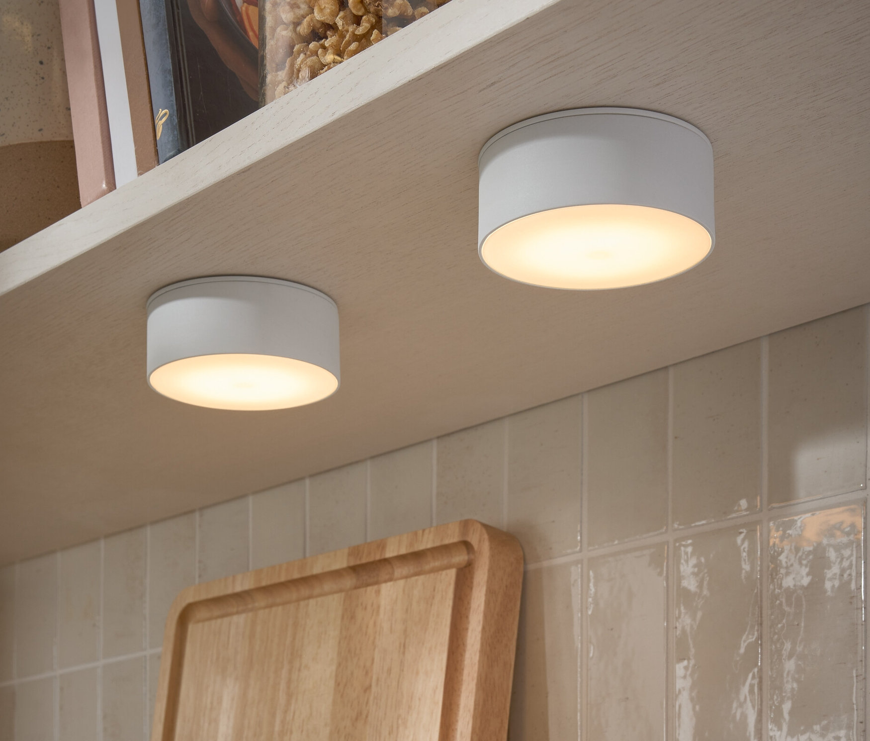 Zwei LED-Multifunktionsleuchten sind an der Unterseite eines Regals befestigt. Auf dem Regal stehen Gläser mit Nüssen und Bücher.