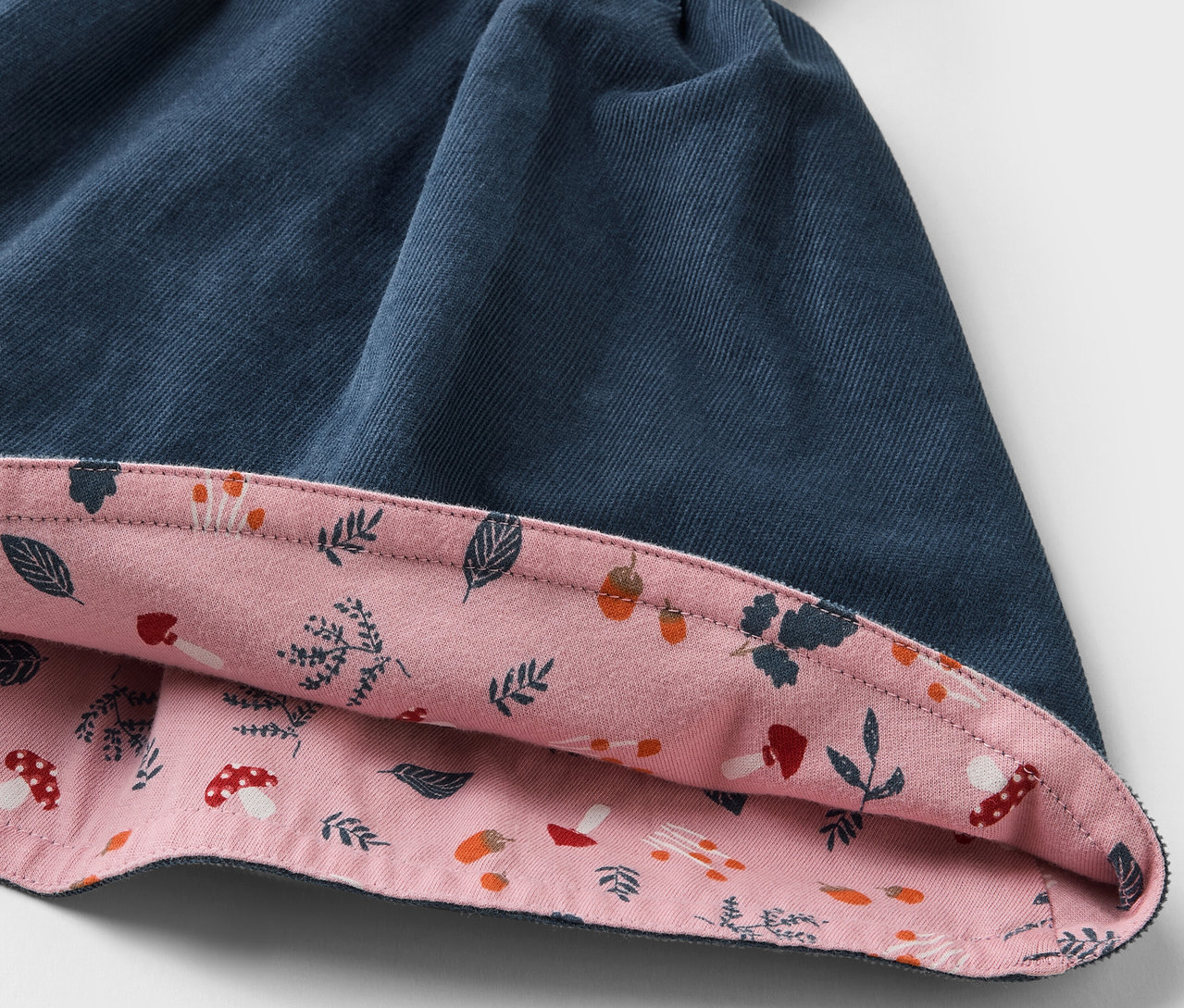 Detailansicht eines Kinder-Cord-Wende-Rocks mit blauer Außenseite und rosa Innenseite mit Blätter- und Pilzaufdruck.