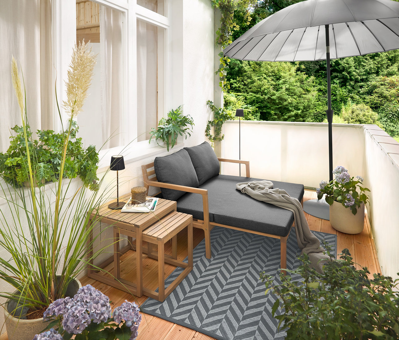 Anordnung auf einem Balkon mit einem ausziehbaren Gartensofa, einem Outdoor-Teppich (ca. 165 x 115 cm), einem flachen Leco Sonnenschirmständer (Ø ca. 60 cm), einem hellgrauen Leco Shanghai Sonnenschirm (Ø 270 cm), einem Balkon Sicht- und Windschutz in Creme, einer schwarzen LED-Akku-Outdoor-Tischleuchte und einer schwarzen LED-Akku-Outdoor-Stehleuchte.