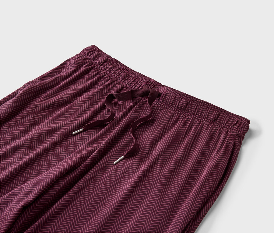 Nahaufnahme einer weinroten Hose mit Kordelzug und Zickzackmuster vor einem weißen Hintergrund.