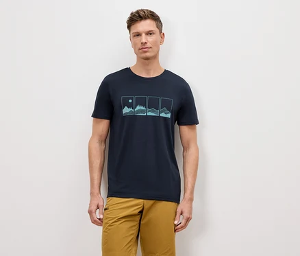 Mann steht vor einer Wand und trägt ein marineblaues T-Shirt mit einer Grafik von vier Naturlandschaften und Khaki-Shorts.