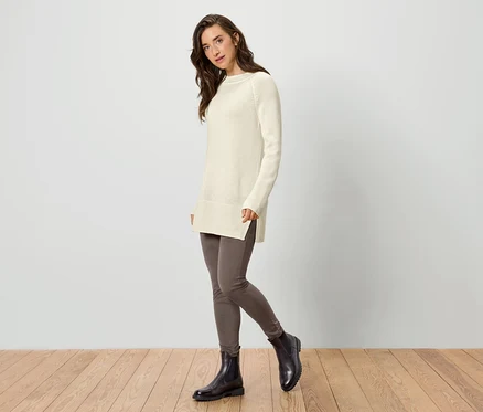 Frau trägt einen langen Strickpullover in Creme, Leggings und Stiefeletten.