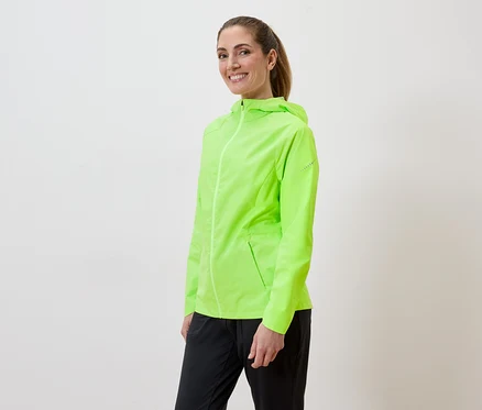Frau mit Pferdeschwanz trägt eine neongrüne Regenjacke und schwarze Hose vor einem weißen Hintergrund.