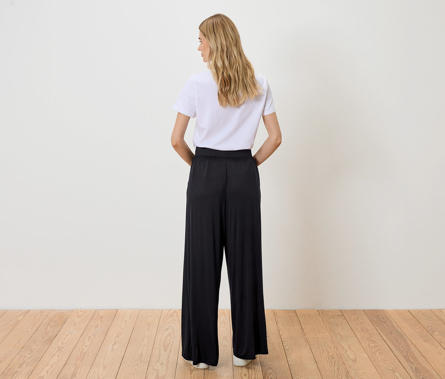 Frau von hinten in weißem T-Shirt und schwarzer Hose.