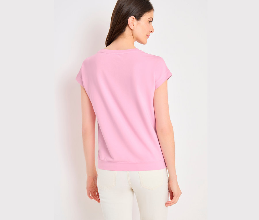 Frau von hinten, trägt ein pinkes CECIL Placement-Shirt und eine helle Hose, blickt nach rechts.