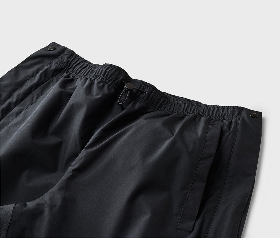 Nahaufnahme einer schwarzen Hose mit elastischem Bund, Kordelzug und Seitentasche vor einem neutralen Hintergrund.
