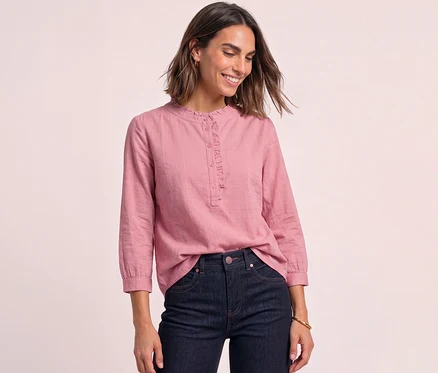 Eine lächelnde Frau trägt eine rosafarbene Street One Cordbluse mit Rüschen und dunkle Jeans.