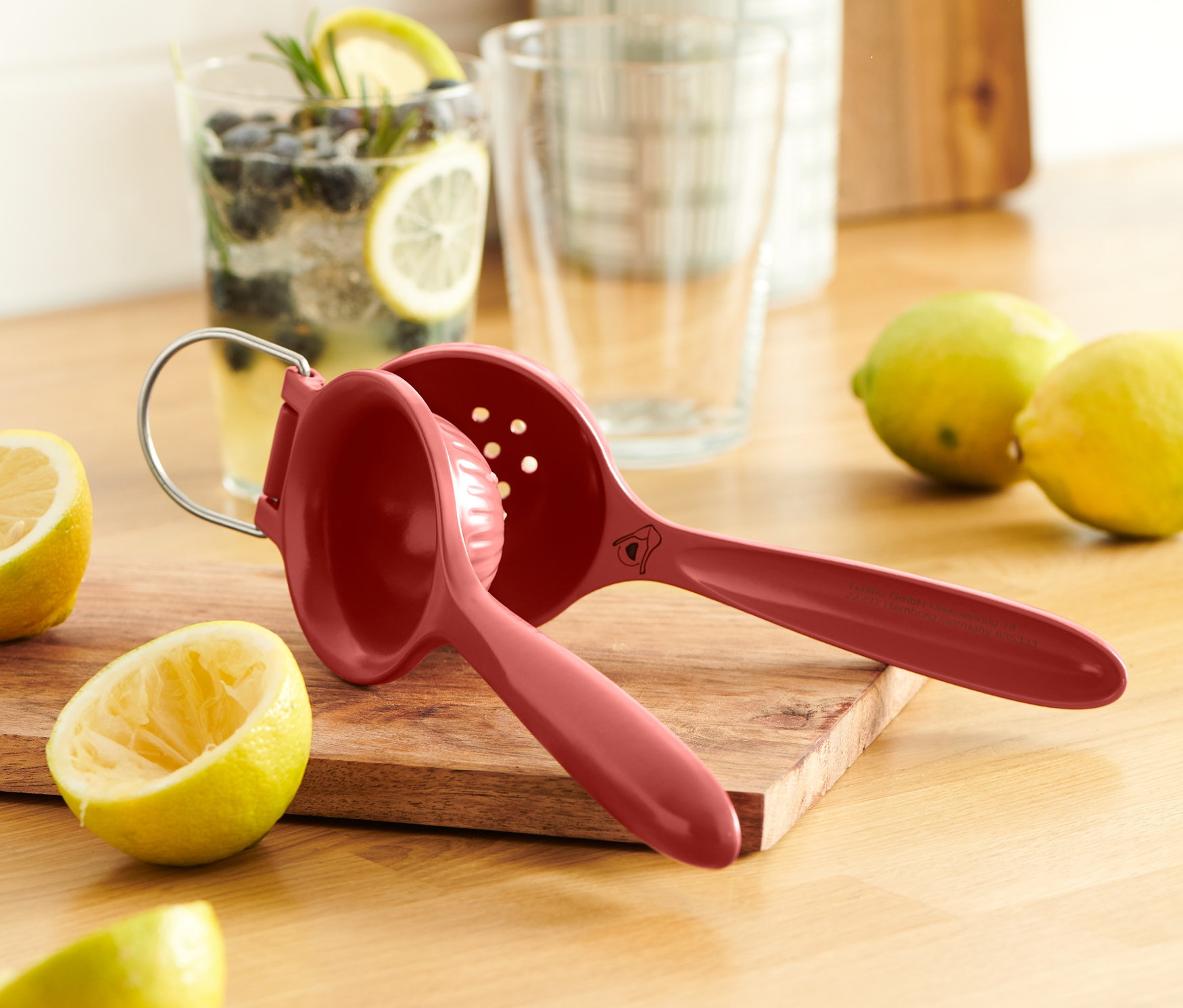 Eine rote Zitruspresse liegt auf einem Holzbrett neben Zitronen.