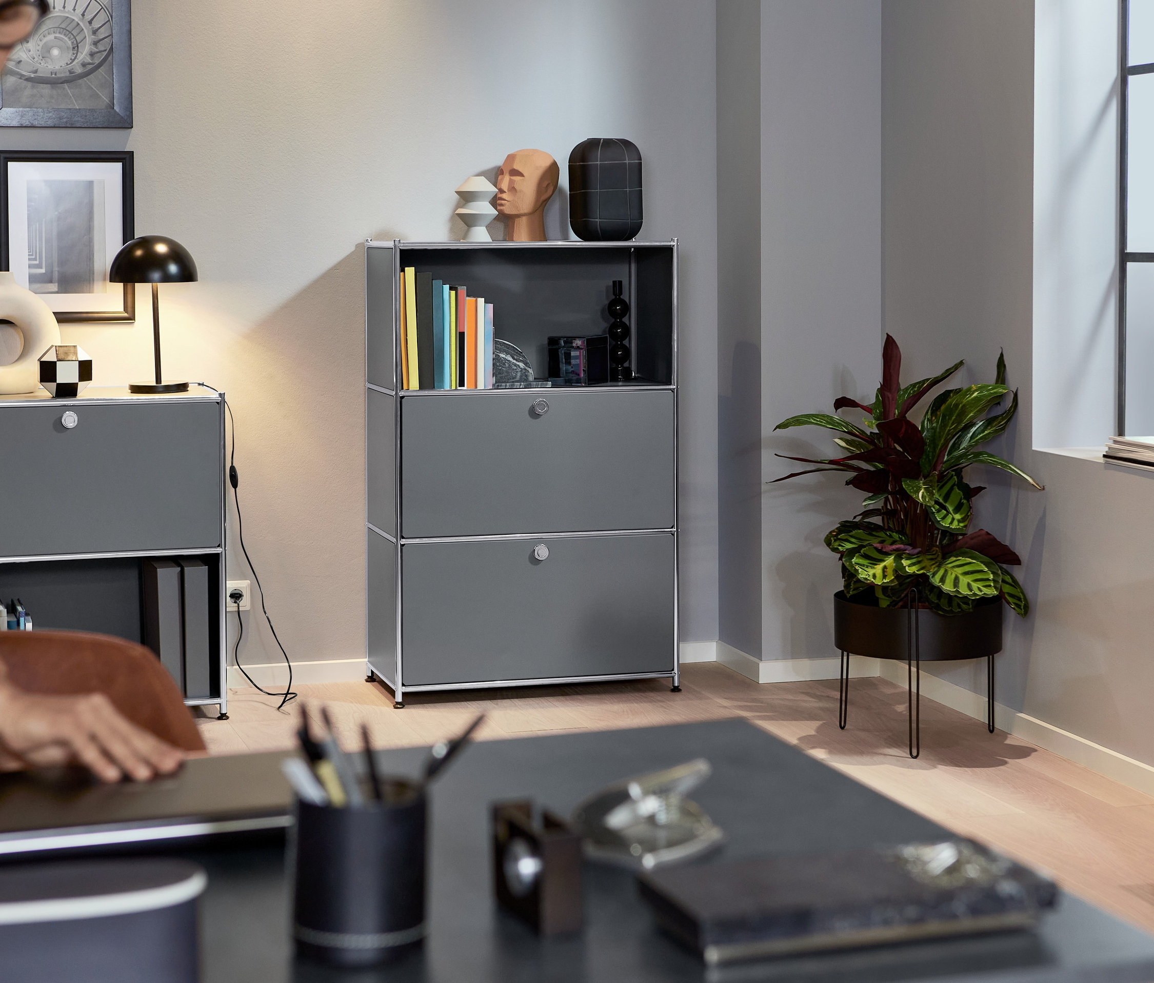 Eine Frau schließt einen Laptop auf einem Tisch. Im Hintergrund befindet sich ein graues Metallregal mit 2 verstellbaren Klappenfächern.