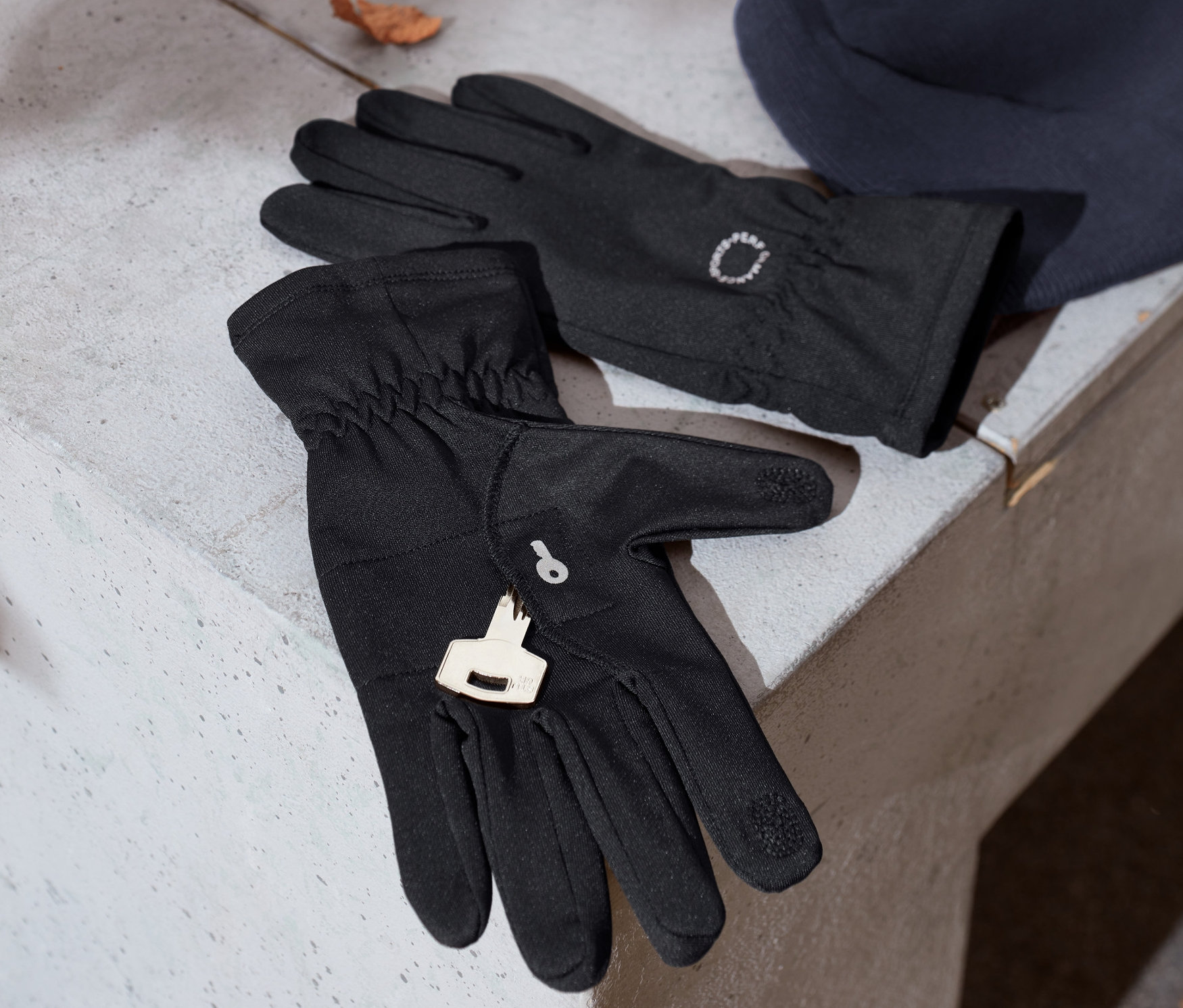 Schwarze Laufhandschuhe mit Reflektorprint liegen neben einer blauen Strickmütze auf einer Betonbank.