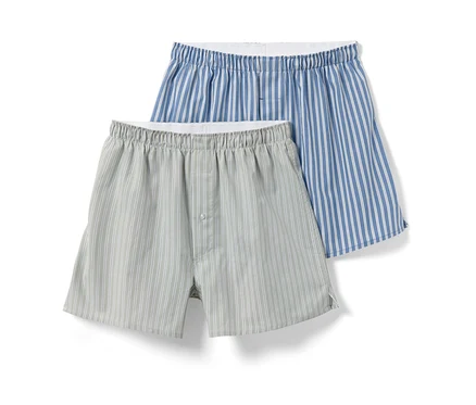Zwei Web-Boxershorts, eine hellgrau mit weißen Streifen und Knopf, die andere blau mit weißen Streifen.