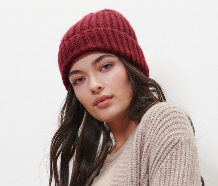 Frau posiert mit Strickmütze mit Wolle, beiger Strickjacke und Jeans.