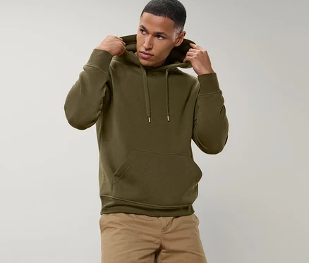 Mann richtet die Kapuze eines olivgrünen Hoodies. Er trägt beige Shorts.