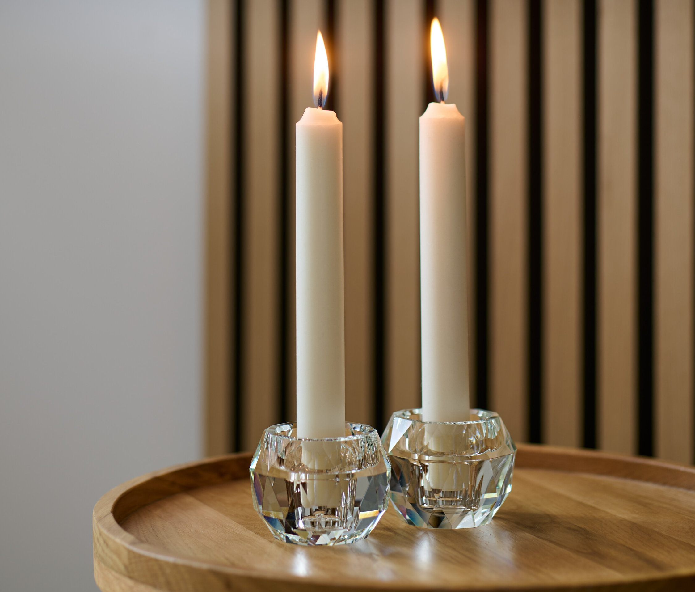 Zwei Glas-Kerzenhalter mit brennenden Kerzen auf einem Holztisch.