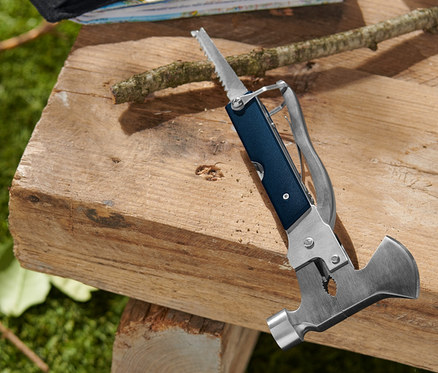 Multifunktionswerkzeug auf einem Holzhocker mit Etui, Karten und einem Zweig.