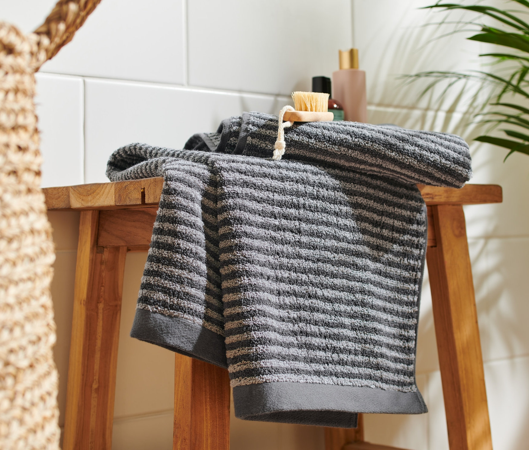 Auf einem Holzschemel liegen zwei hochwertige anthrazitfarbene Handtücher.