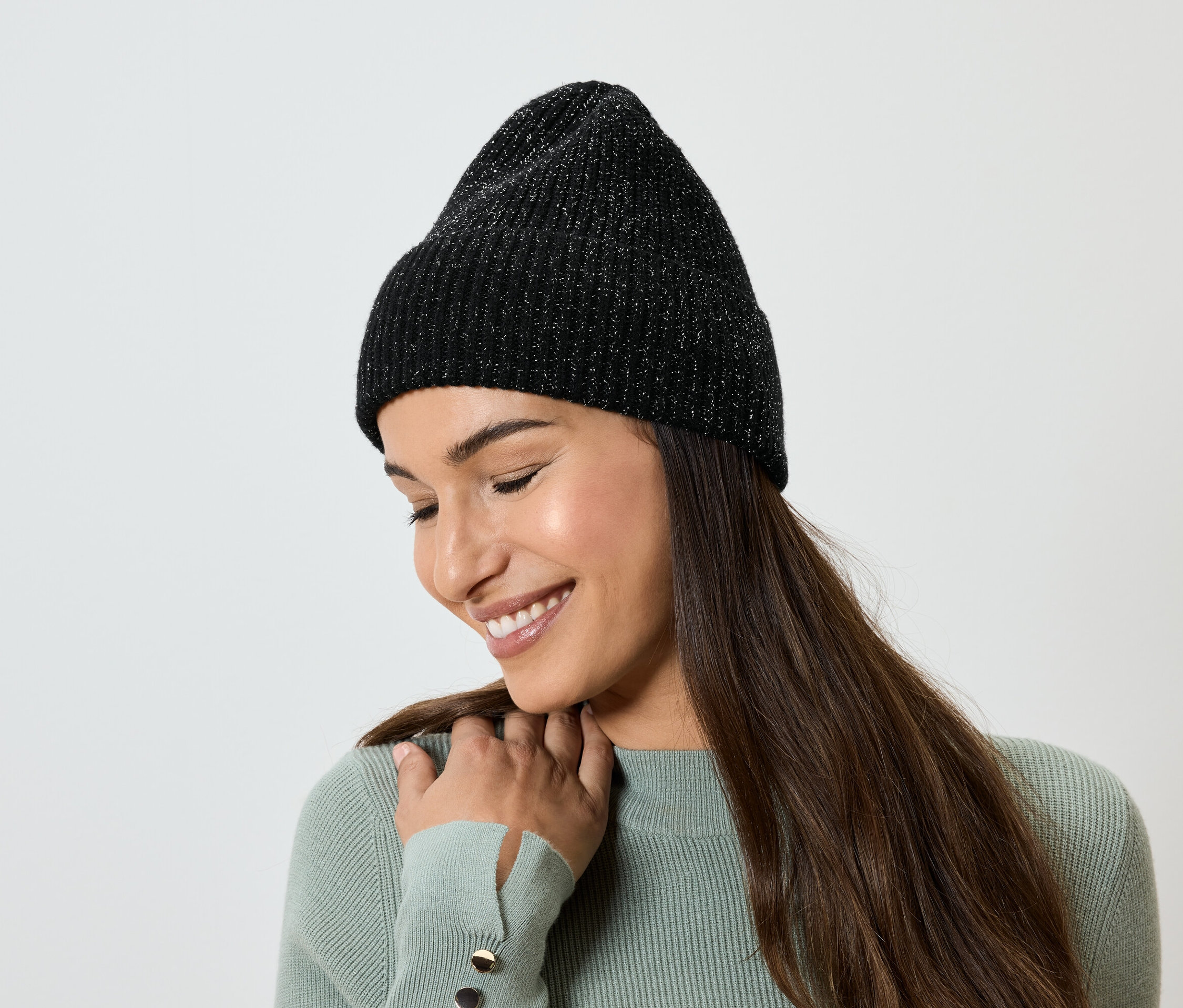 Frau mit langen braunen Haaren lächelt und trägt eine schwarze Strickmütze.