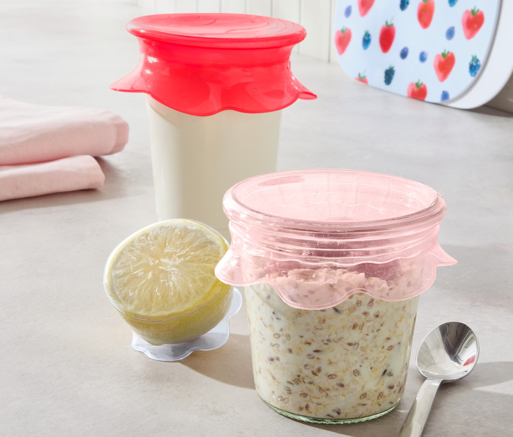 Zwei Gläser mit Inhalt sind mit 3 Silikon-Frischhaltedeckeln abgedeckt. Daneben liegen eine Zitrone und ein Löffel.