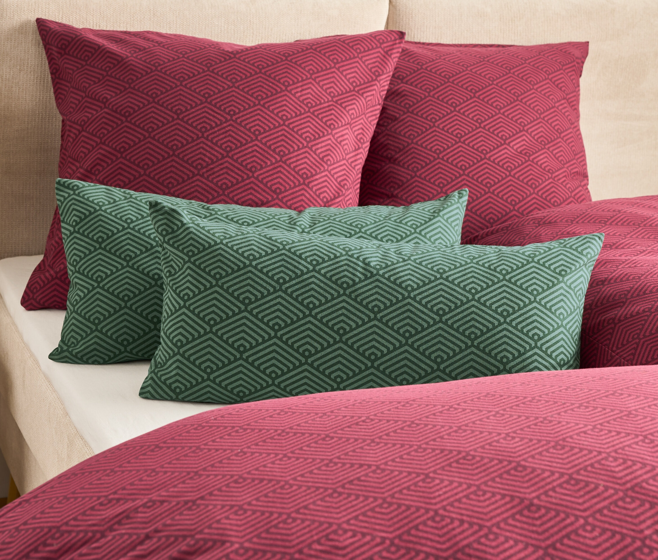 Auf einem Bett liegen zwei weinrote und zwei grüne Kissen mit geometrischem Muster.
