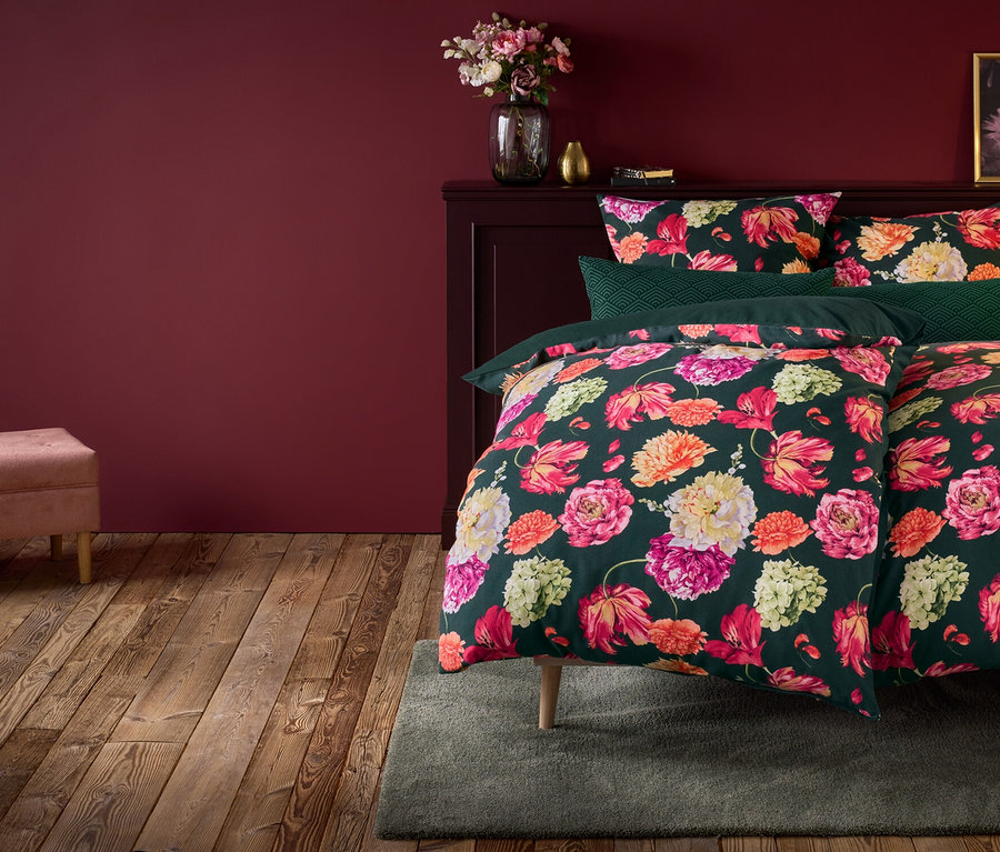 Blumenbettwäsche auf Bett mit Nachttisch, Lampe und rosa Bank.