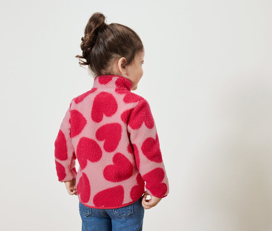 Kleines Mädchen mit einem Sweatshirt mit roten Herzen, das nach rechts schaut.