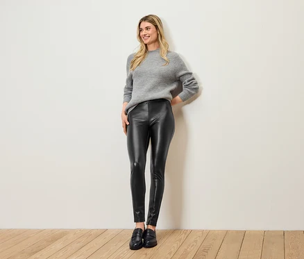 Frau posiert mit grauem Pullover, schwarzen Lederleggings und schwarzen Schuhen.