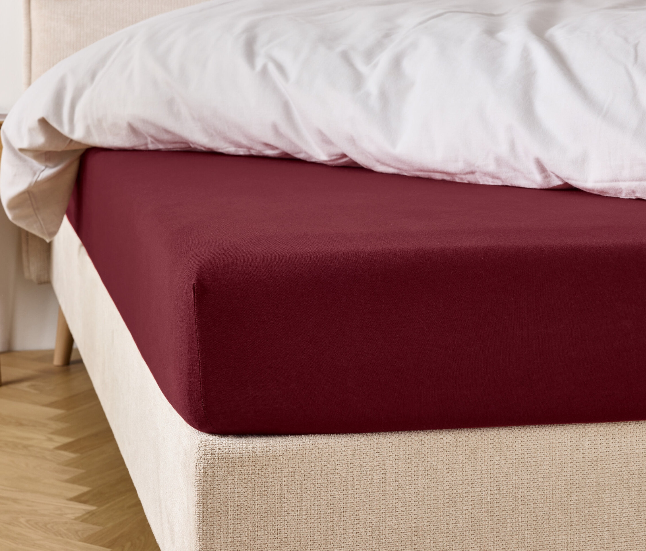 Weinrotes Spannbettlaken auf einem Bett mit weißer Bettdecke.