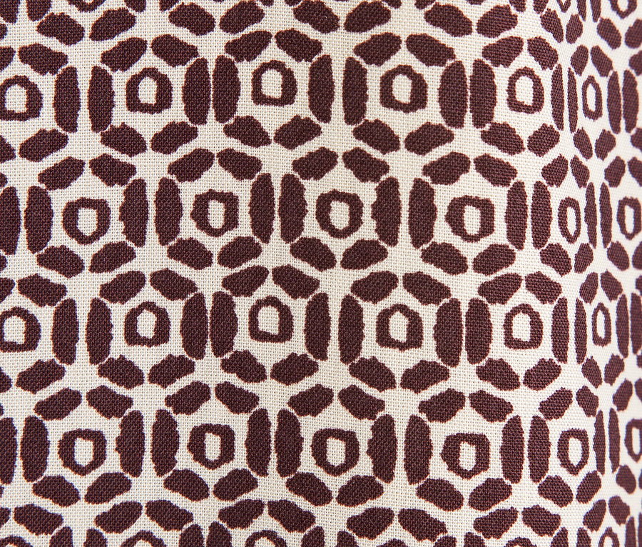 Detailaufnahme eines Stoffes mit braunem geometrischem Muster auf beigem Hintergrund.