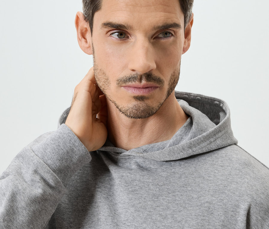 Nahaufnahme eines Mannes mit grauem Kapuzenpullover, die Hand am Nacken.