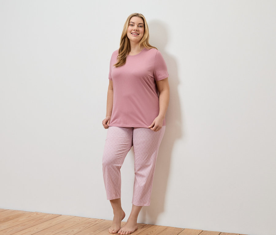 Frau mit langen blonden Haaren, die ein rosafarbenes T-Shirt und eine rosafarbene Hose mit geometrischem Muster trägt.