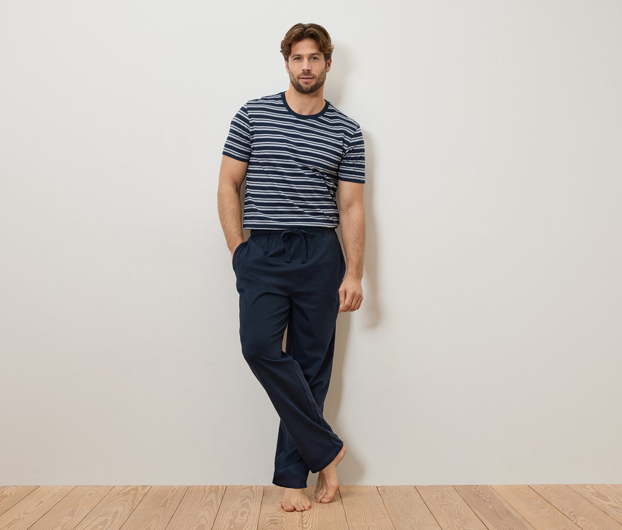 Mann lehnt an einer Wand, trägt ein blau-weiß gestreiftes T-Shirt und eine marineblaue Pyjamahose.