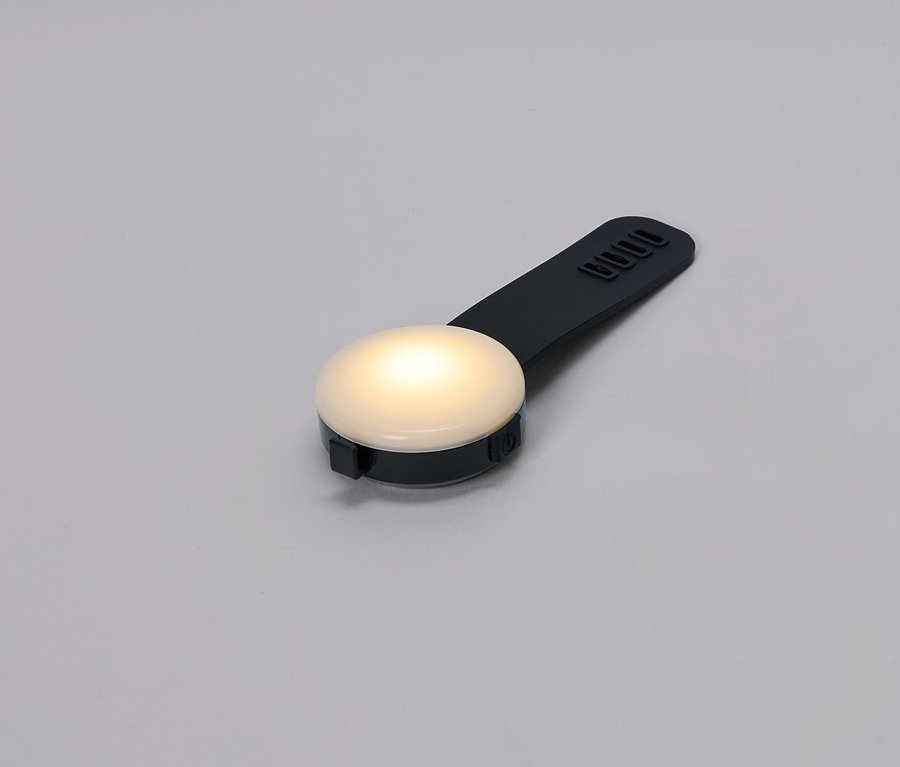 Nahaufnahme einer kleinen, runden, leuchtenden Lampe mit einem schwarzen Griff auf grauem Hintergrund.