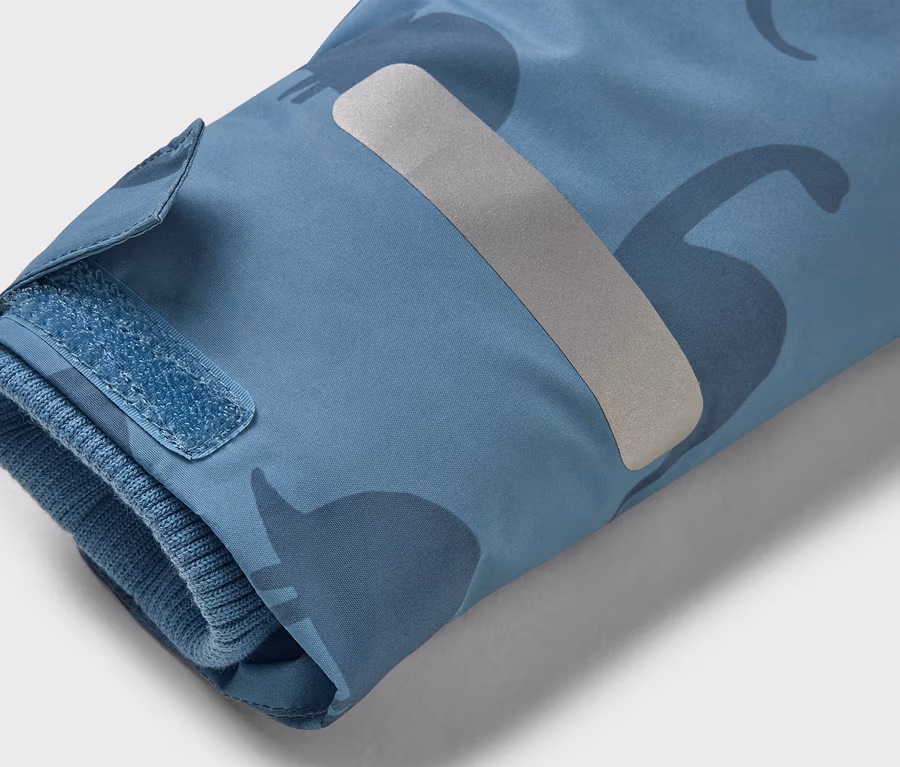 Nahaufnahme des Ärmels einer hellblauen Jacke mit Dinosaurier-Muster, Klettverschluss und reflektierendem Streifen.