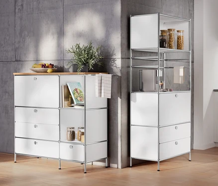 Im Raum stehen ein Sideboard Metall »CN3« mit Holzplatte, 1 Klappenfach und 4 Schubladen, weiß und ein Regal Metall »CN3« mit 1 Klappenfach und 2 Schubladen.